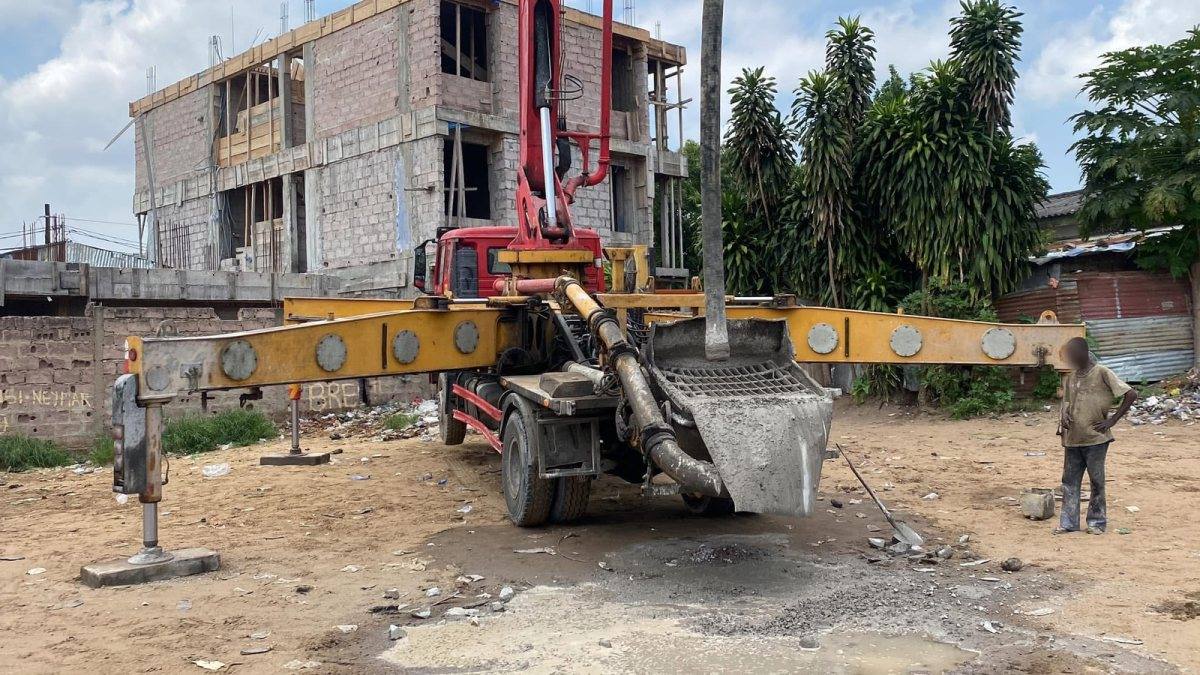 Camion pompe à béton aux stabilisateurs déployés devant un immeuble en construction