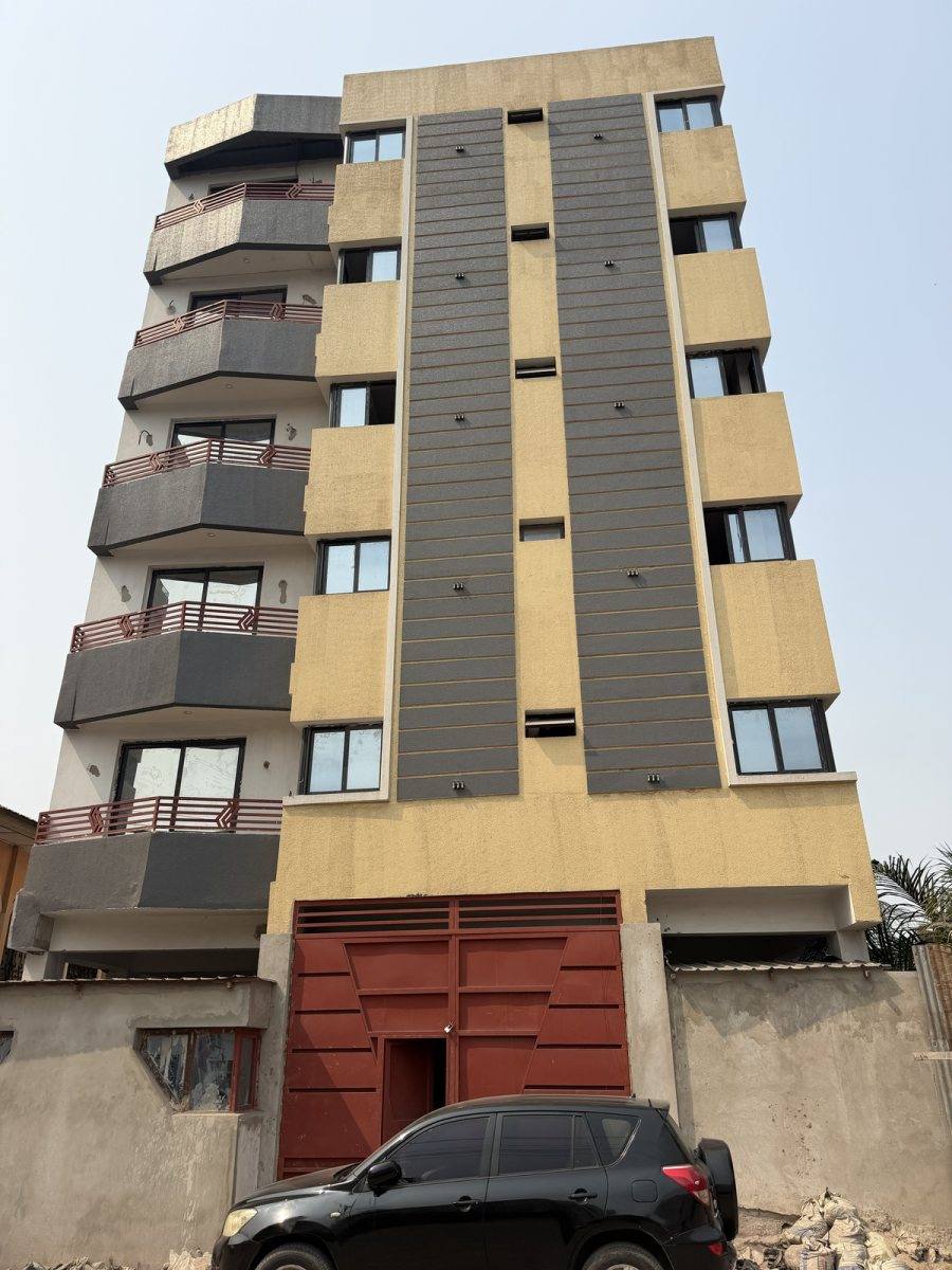 Immeuble de plusieurs niveaux achevé, façade jaune et grise, balcons à garde-corps rouges et portail rouge