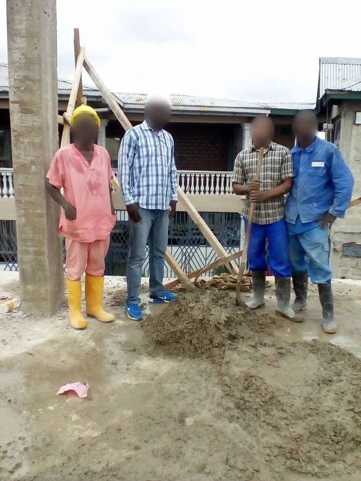 Quatre hommes autour d'un tas de mortier sur une dalle, près d'un poteau en béton
