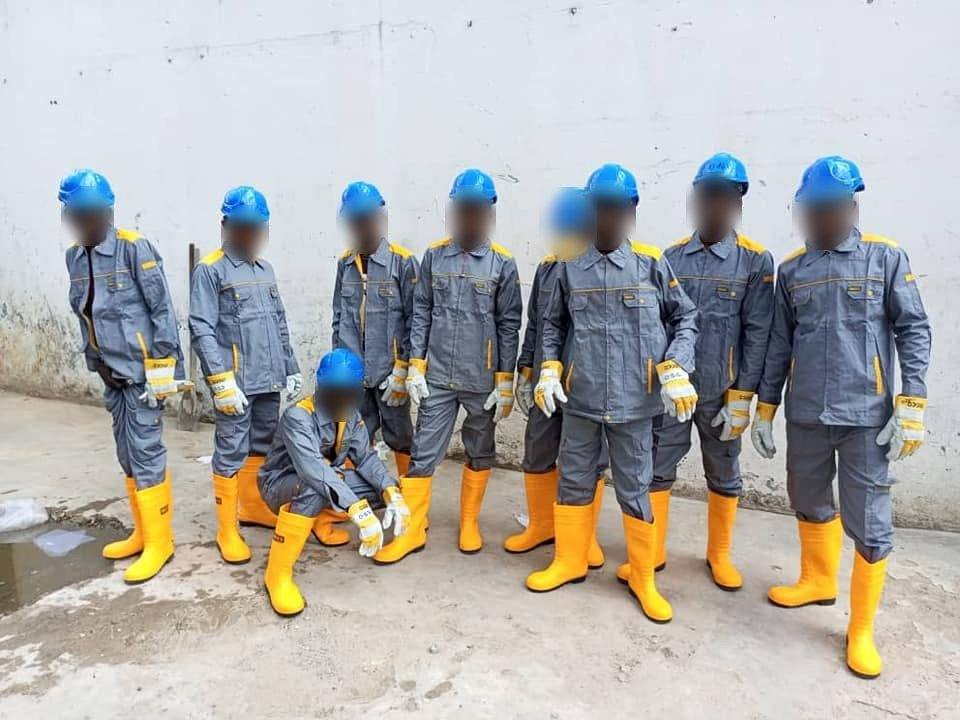 Équipe d'ouvriers en tenue grise, casques bleus et bottes jaunes devant un mur